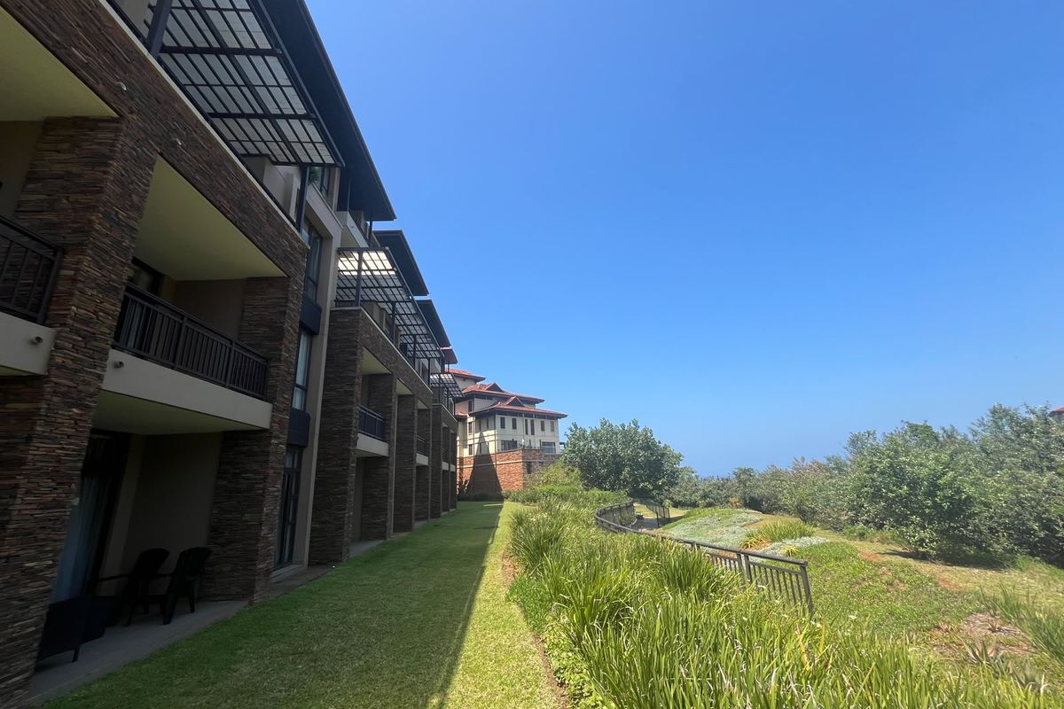 Rear view of the apartment complex featuring stone-clad facades, private balconies with metal railings, and well-maintained landscaped garden areas.