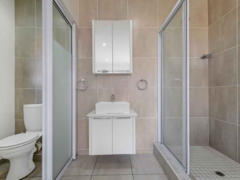 A modern, clean bathroom featuring a wall-mounted vanity with a vessel sink, a mirrored medicine cabinet, and a separate glass-enclosed shower.
