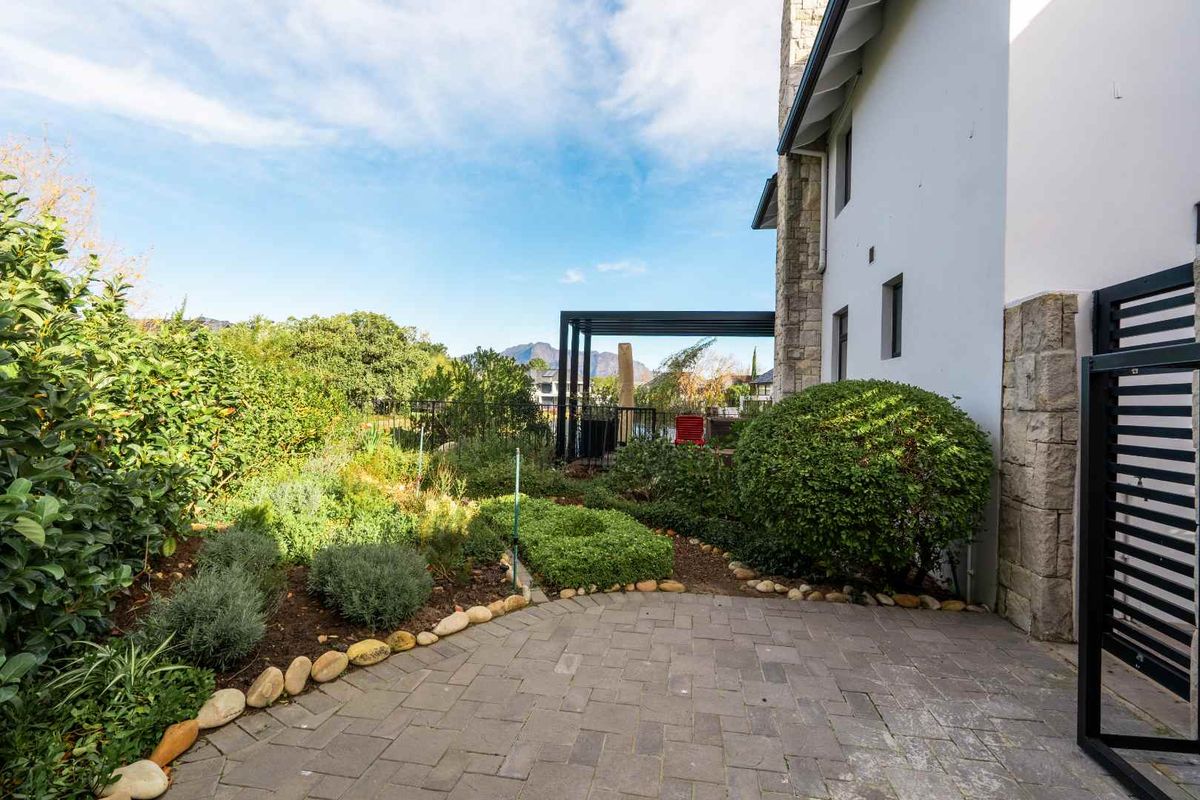A well-maintained rear garden featuring a paved patio area, stone-clad building exterior, and a modern pergola structure.