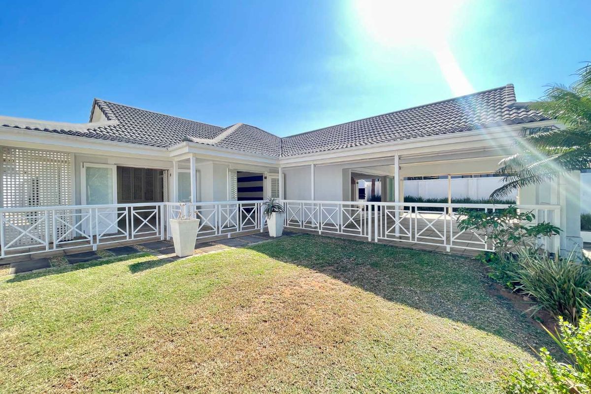 A well-maintained rear exterior view featuring a covered patio area with white balustrades, tiled roof, and a landscaped garden.
