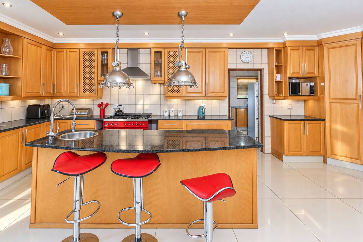 Spacious kitchen featuring warm wooden cabinetry, granite countertops, a central island with breakfast bar, and integrated appliances, leading into a secondary scullery area.