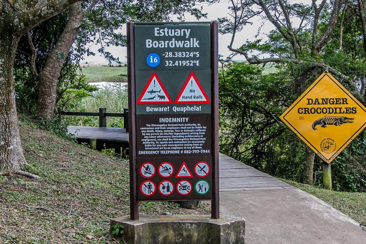 A view of the Estuary Boardwalk entrance featuring safety signage and a wooden walkway leading into the natural surroundings.