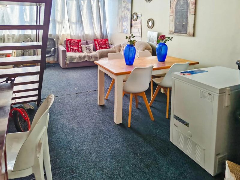 Open plan living and dining area featuring carpeted flooring and large windows, offering a versatile space for relaxation and meals.