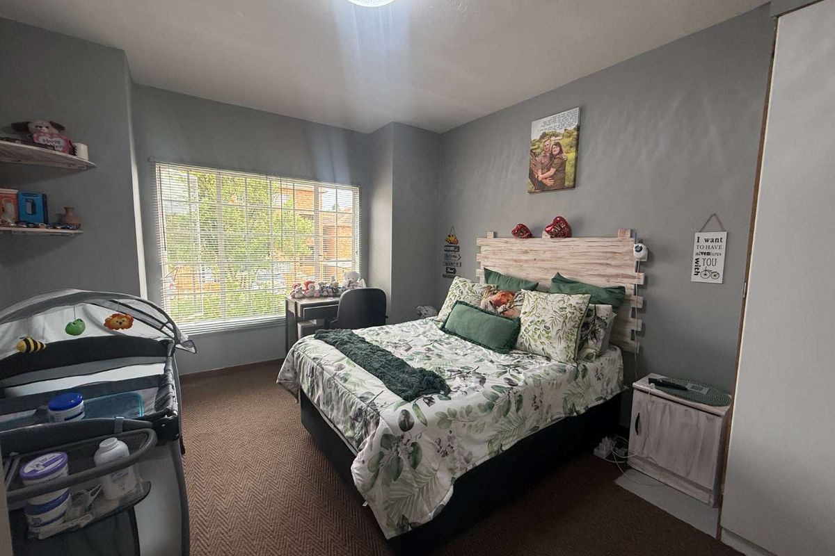 A well-lit bedroom featuring neutral grey walls, carpeted flooring, and a large window providing natural light.