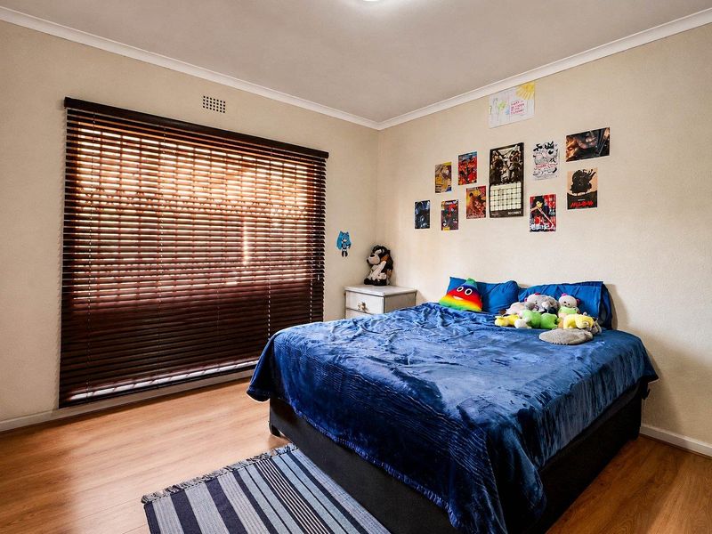 A standard bedroom featuring laminate flooring, neutral wall finishes, and dark wood venetian blinds, providing a functional and well-lit sleeping space.