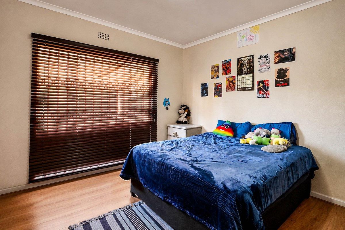 A standard bedroom featuring laminate flooring, neutral wall finishes, and dark wood venetian blinds, providing a functional and well-lit sleeping space.