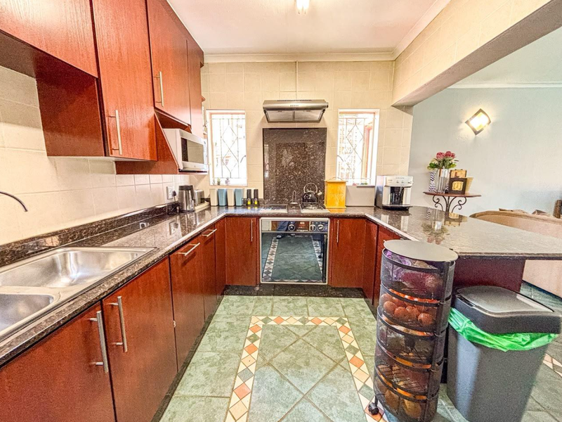 A functional kitchen featuring dark wood cabinetry, granite countertops, a built-in oven with hob, and a double bowl sink with tiled flooring.