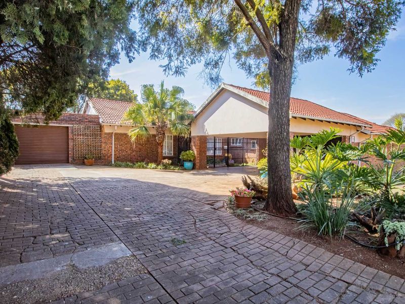 Front exterior view of the property featuring a spacious brick-paved driveway, a garage, and a covered carport area with mature garden landscaping.