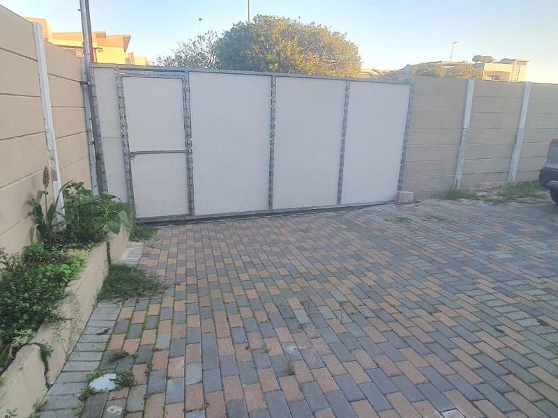A paved driveway area featuring a sliding gate, precast concrete boundary walls, and a raised planter bed.