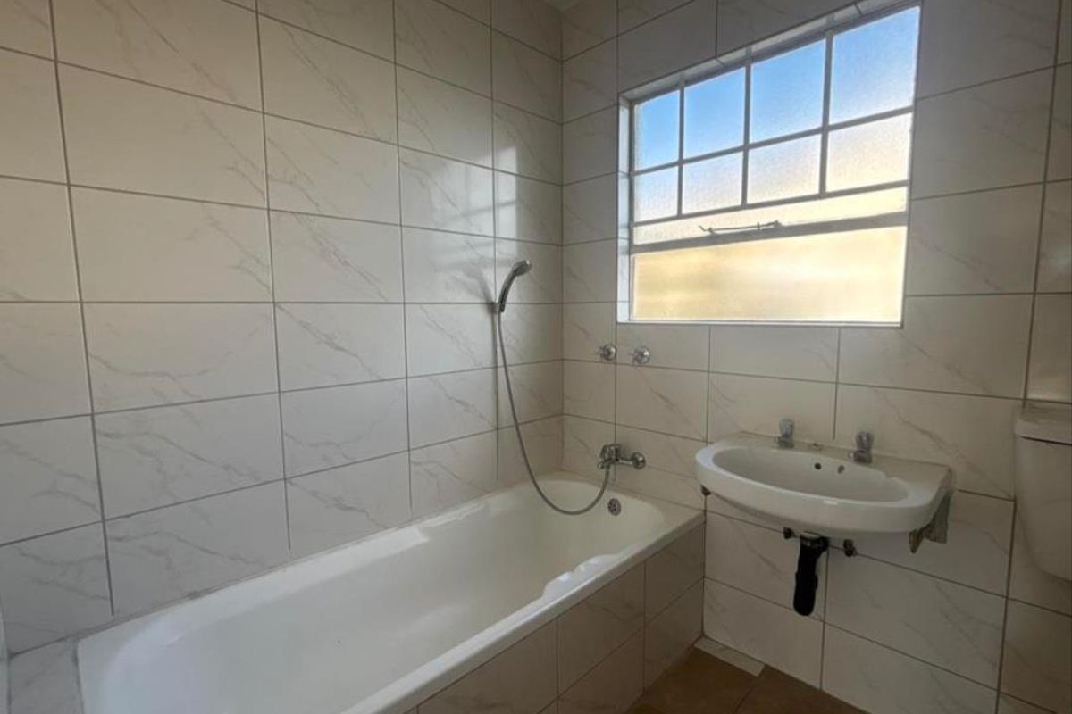 A functional bathroom featuring a bathtub with handheld shower attachment, wall-mounted basin, and tiled walls with a window for natural light.