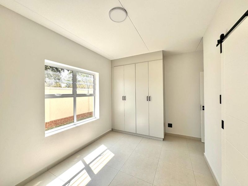 A bright, empty bedroom featuring neutral tiled flooring, built-in cupboards, and a modern sliding barn door, offering a clean and versatile living space.