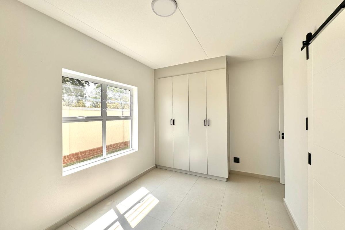 A bright, empty bedroom featuring neutral tiled flooring, built-in cupboards, and a modern sliding barn door, offering a clean and versatile living space.