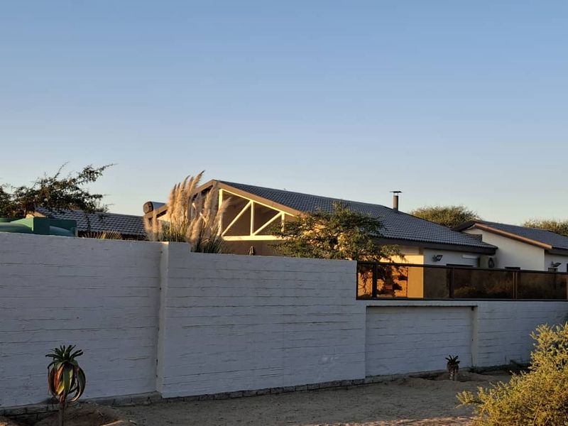 A view of the property exterior featuring a white perimeter wall, tiled roof with solar water heating, and a modern glass balustrade section.