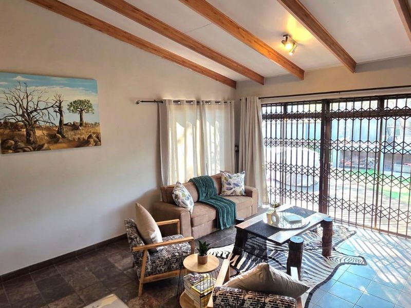 A cozy living room featuring exposed timber ceiling beams, tiled flooring, and a sliding glass door with a security gate leading to the exterior.