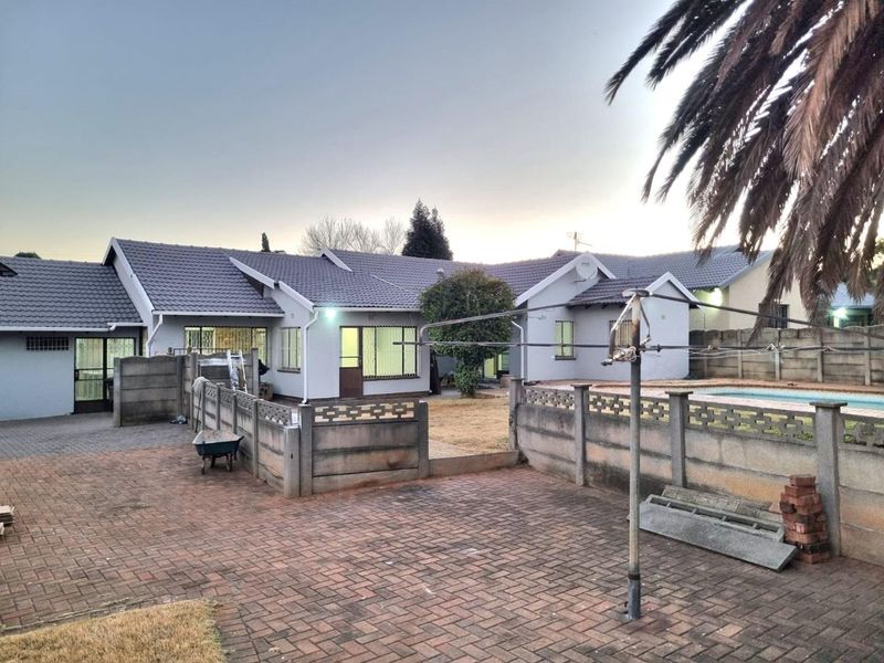 Rear view of the property featuring a paved courtyard, swimming pool, and precast boundary wall with a tiled roof house structure.