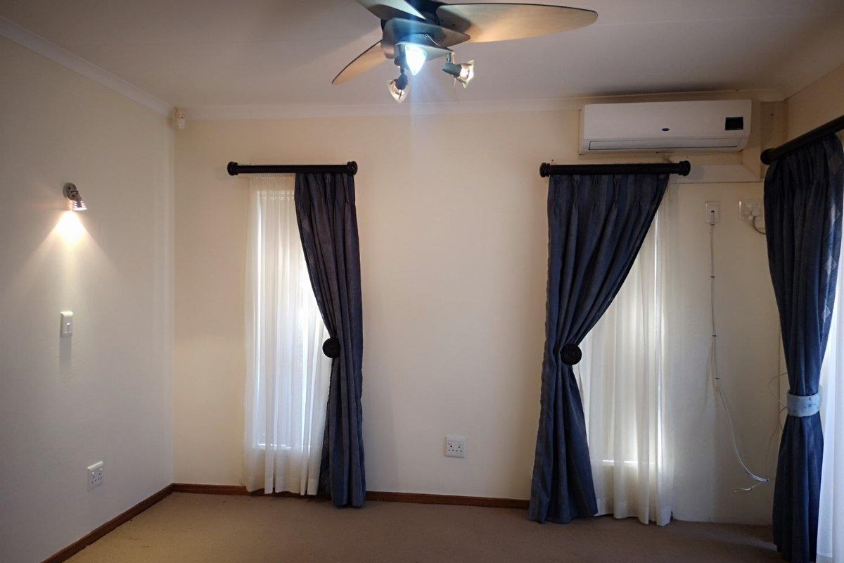 A bedroom featuring a ceiling fan, wall-mounted air conditioning unit, and dual windows with curtains.