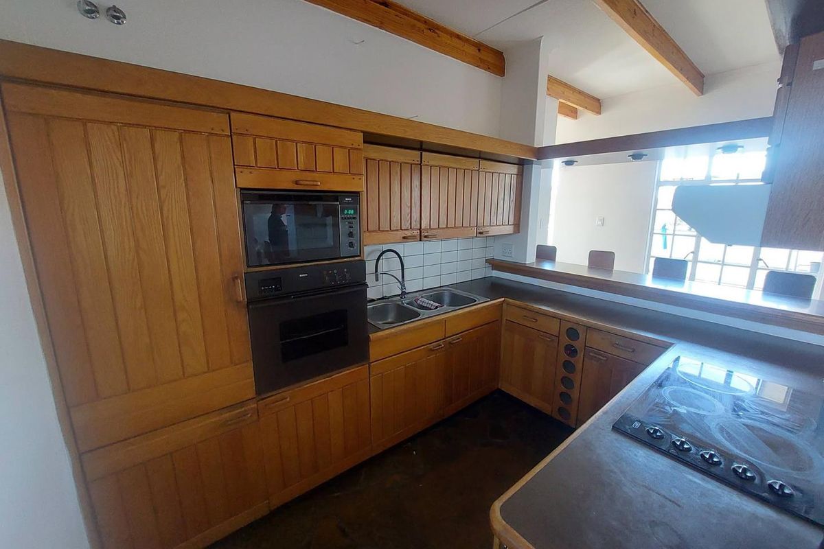 A functional kitchen featuring extensive wooden cabinetry, built-in appliances, a double sink, and a breakfast bar, complemented by exposed timber ceiling beams.