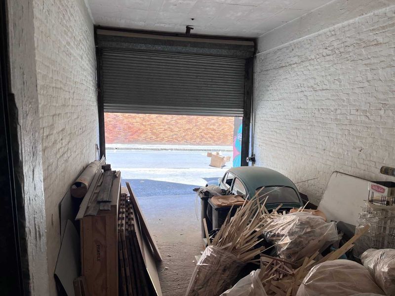 Industrial garage space featuring exposed brick walls, a concrete floor, and a functional roller shutter door opening to the street.