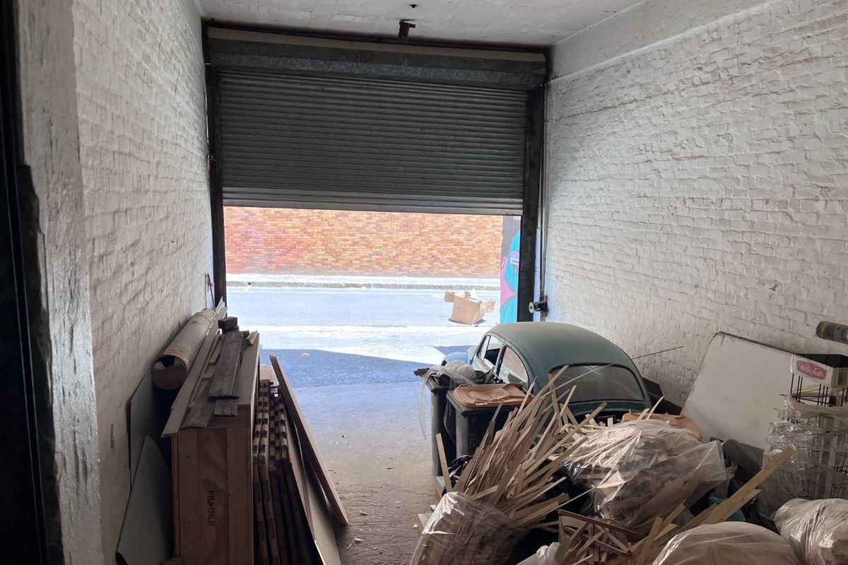 Industrial garage space featuring exposed brick walls, a concrete floor, and a functional roller shutter door opening to the street.