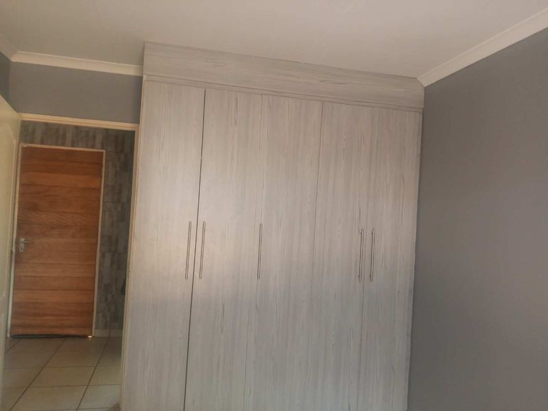 A bedroom featuring modern light wood-grain built-in cupboards and neutral grey wall finishes.