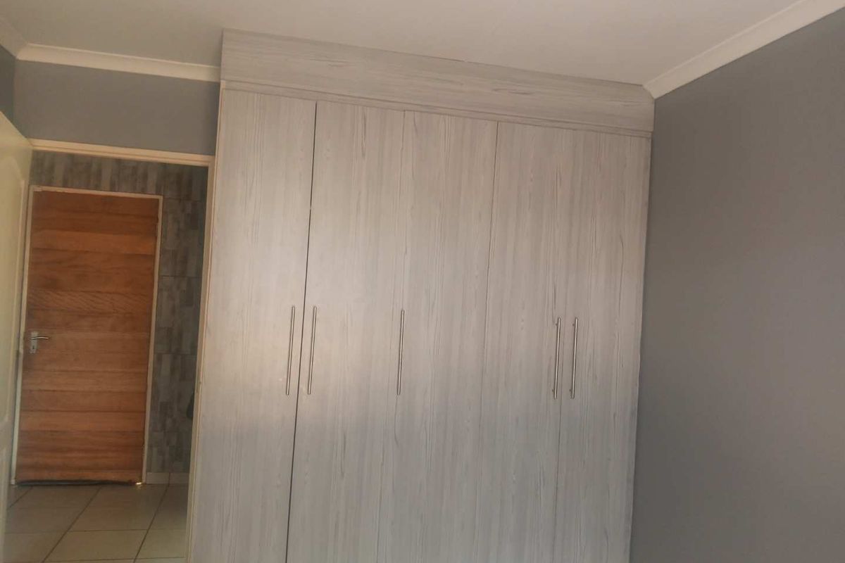A bedroom featuring modern light wood-grain built-in cupboards and neutral grey wall finishes.