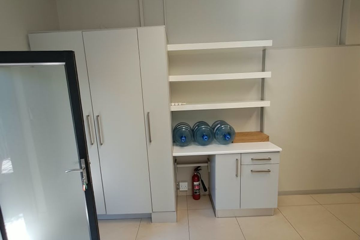 A clean, functional office space featuring built-in storage cabinetry, open shelving, tiled flooring, and a suspended ceiling.