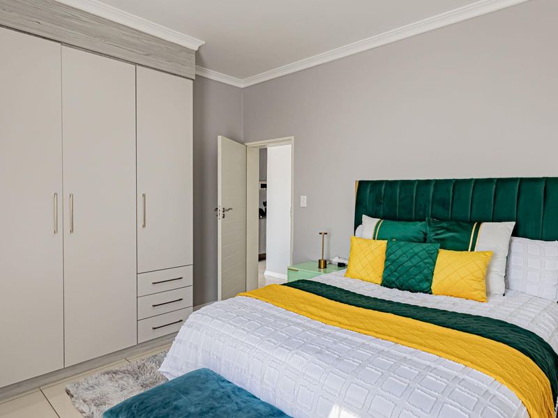 A well-maintained bedroom featuring neutral walls, crown molding, tiled flooring, and ample built-in cupboard storage.