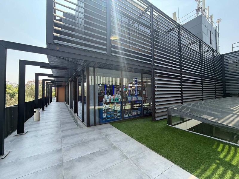Modern retail storefront featuring a large glass facade, metal louvre screening, and a clean tiled walkway with integrated artificial turf landscaping.