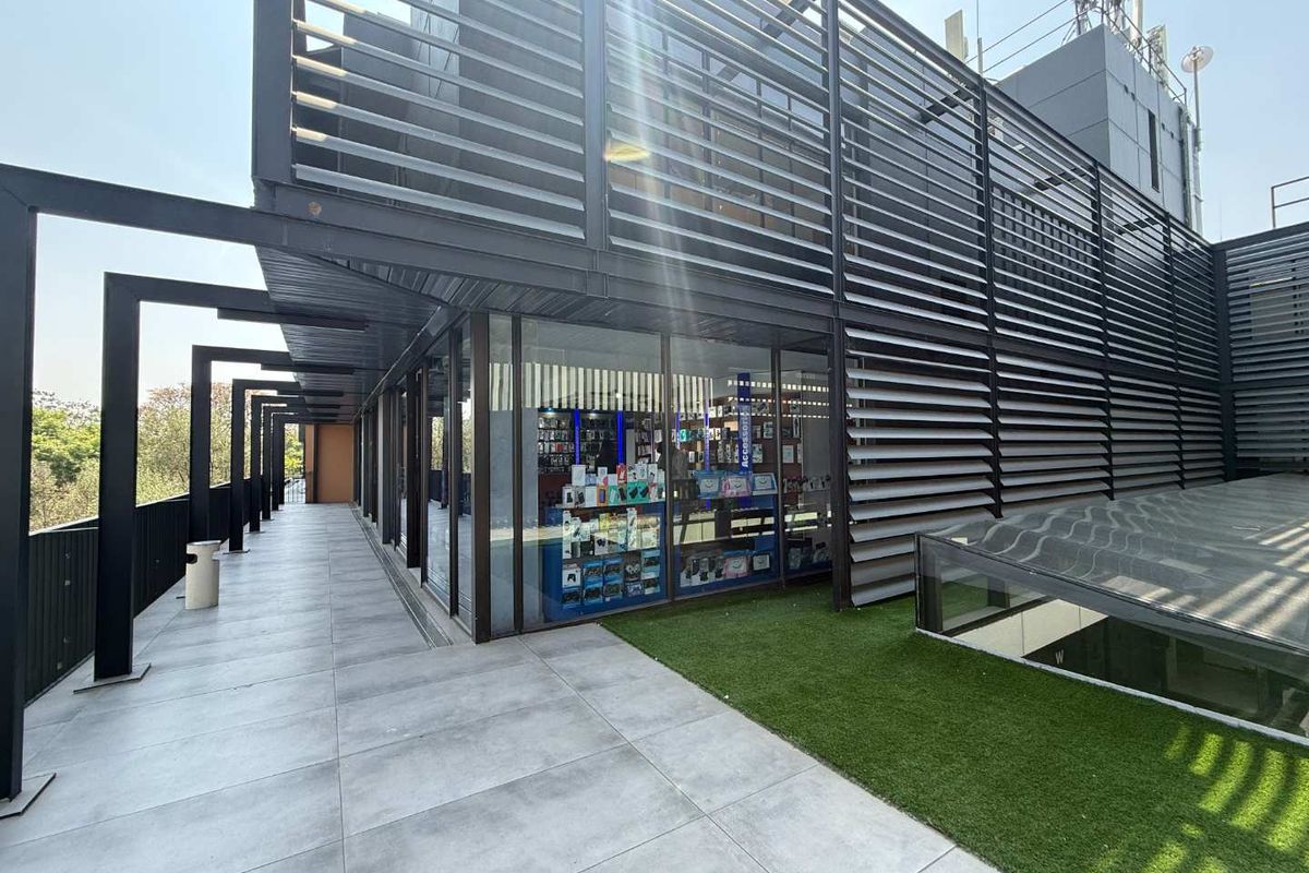 Modern retail storefront featuring a large glass facade, metal louvre screening, and a clean tiled walkway with integrated artificial turf landscaping.