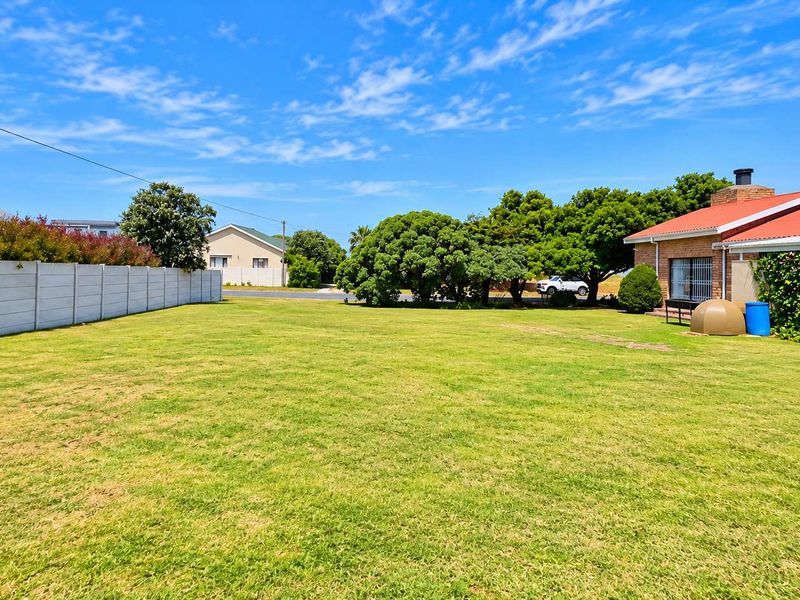 A spacious, well-maintained residential garden featuring a large lawn, mature trees, and a secure precast concrete boundary wall.