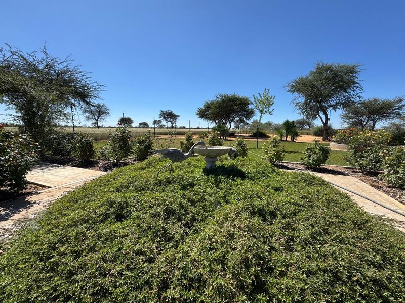 A well-maintained garden area featuring paved pathways, a central stone bird bath, and established landscaping with views of the surrounding farm landscape.