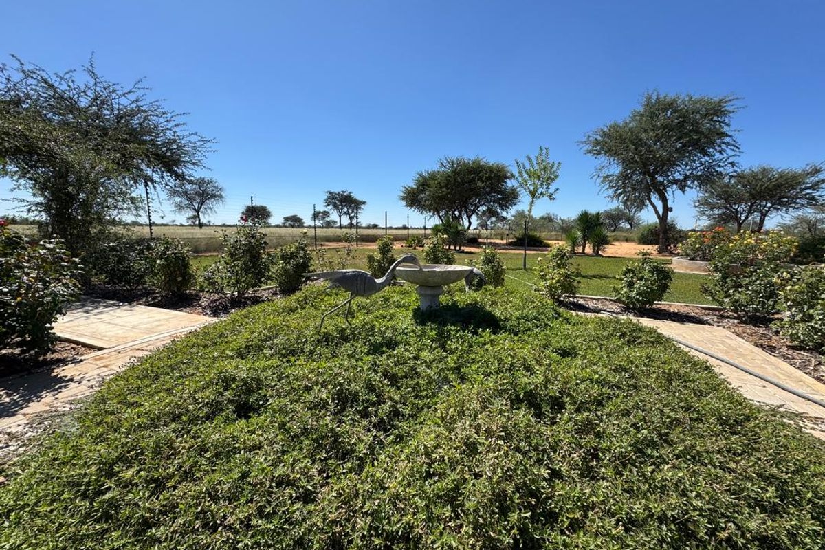 A well-maintained garden area featuring paved pathways, a central stone bird bath, and established landscaping with views of the surrounding farm landscape.