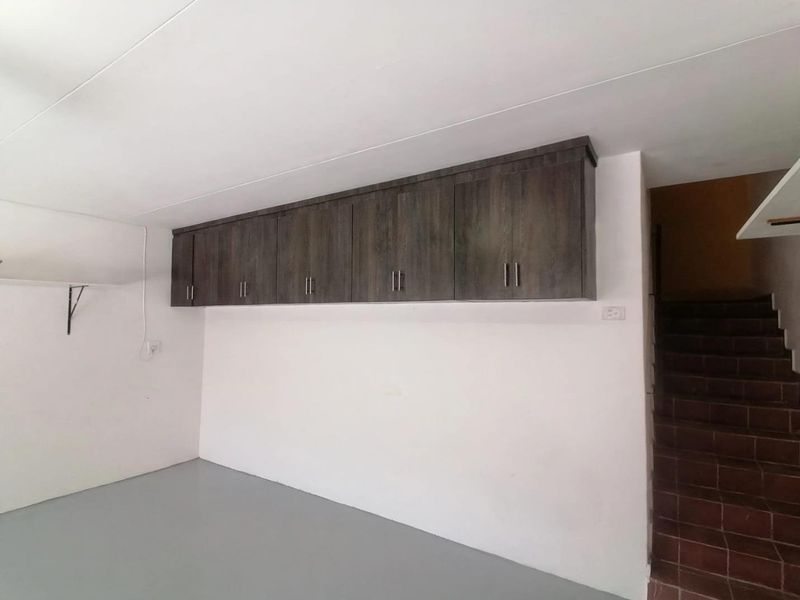 A clean, empty garage space featuring built-in overhead storage cabinetry and a tiled staircase leading to the upper level.