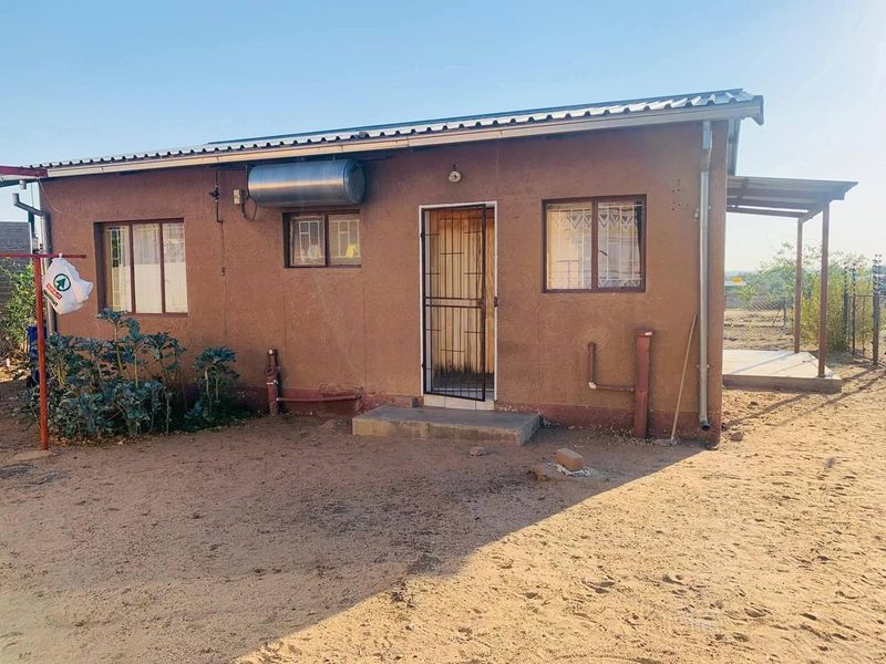 Rear view of a single-story house featuring a solar water heater, security gate, and metal window frames with a basic exterior finish.