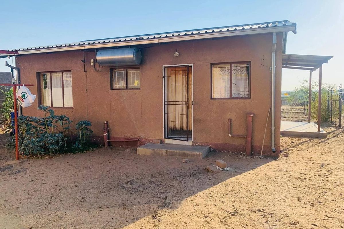 Rear view of a single-story house featuring a solar water heater, security gate, and metal window frames with a basic exterior finish.