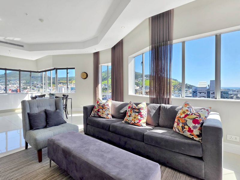 Bright open-plan living area featuring expansive windows with panoramic city and mountain views, modern tiled floors, and recessed ceiling lighting.
