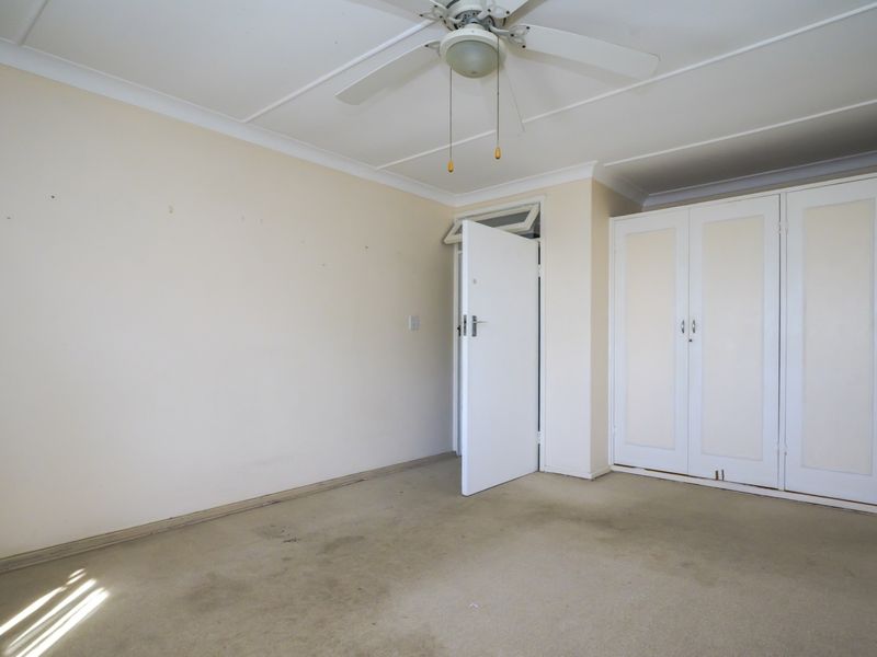 An empty bedroom featuring built-in cupboards, a ceiling fan, and carpeted flooring, offering a blank canvas for renovation or restyling.