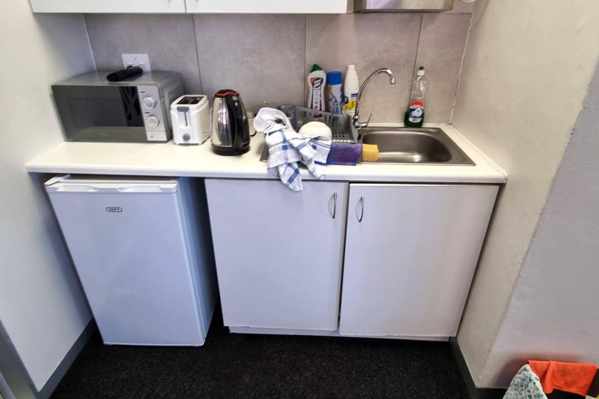A compact kitchenette area featuring a stainless steel sink, white cabinetry, and tiled backsplash, suitable for office use.