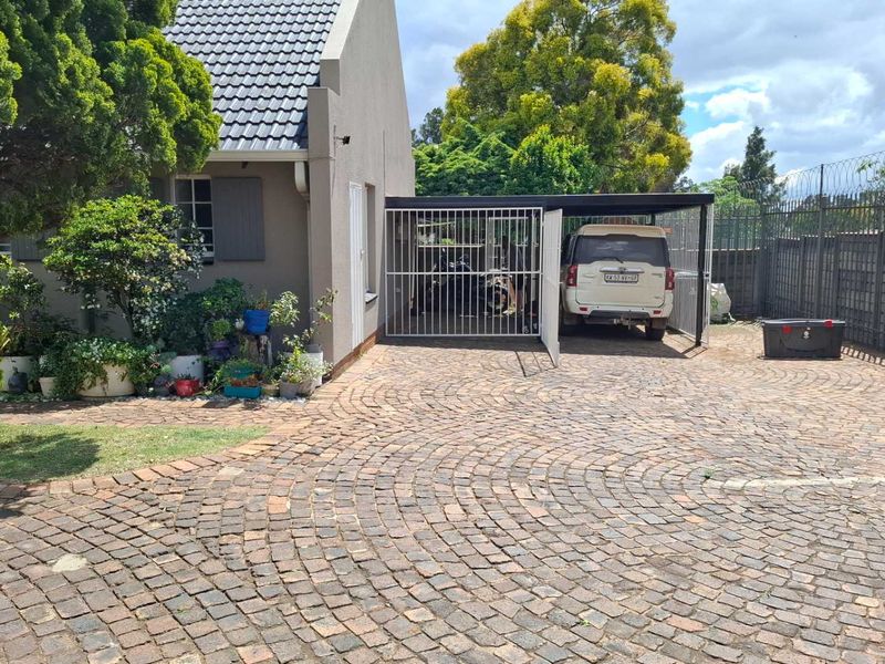 Front exterior view of the townhouse featuring a paved cobblestone driveway, a covered carport, and secure perimeter fencing.