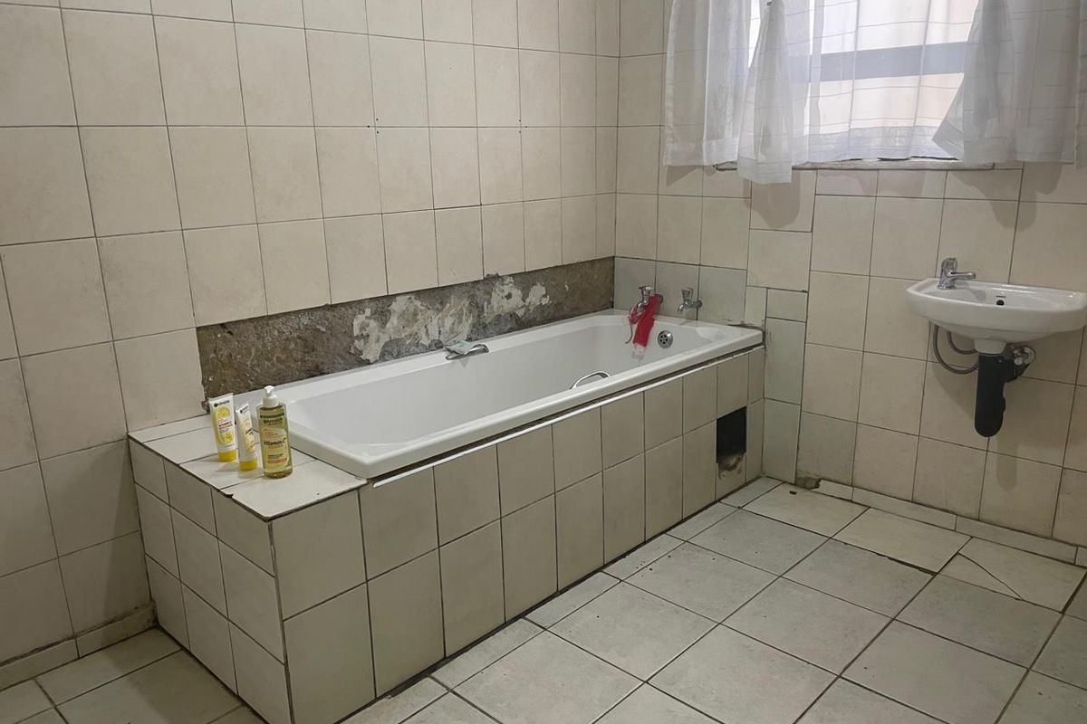 A dated bathroom featuring a tiled bathtub surround, wall-mounted basin, and ceramic floor tiles, currently requiring maintenance and cosmetic repairs to the wall finishes.