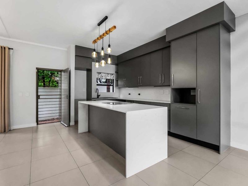 Modern kitchen featuring sleek grey cabinetry, a central island with a white quartz countertop, and contemporary pendant lighting.