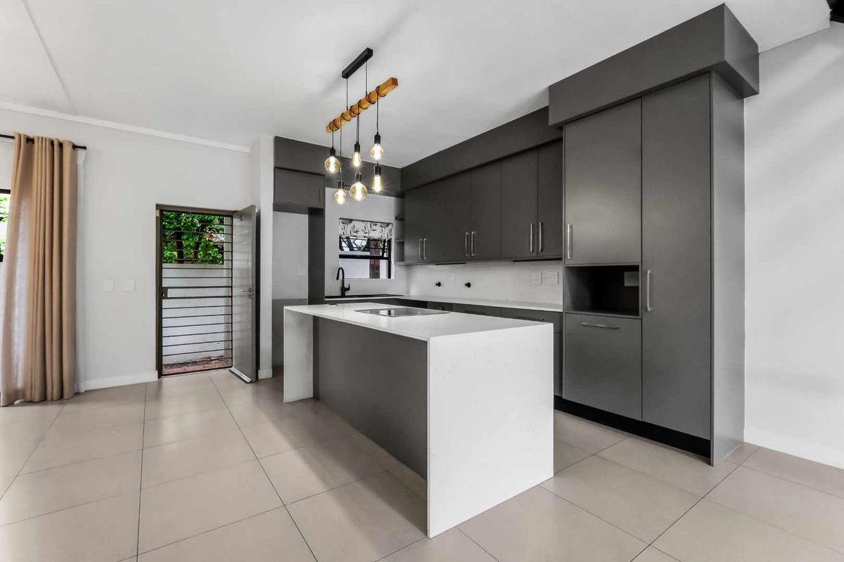 Modern kitchen featuring sleek grey cabinetry, a central island with a white quartz countertop, and contemporary pendant lighting.