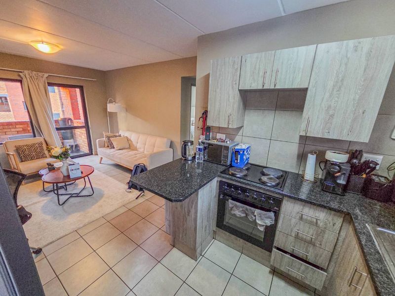 Open-plan living area featuring a compact kitchen with granite countertops, electric hob, and oven, flowing into a lounge space with access to a balcony.