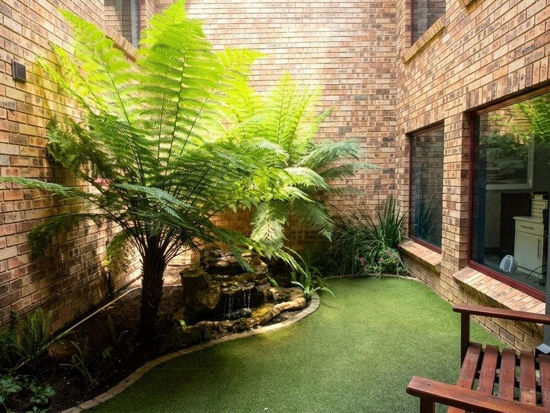 A private courtyard featuring brick walls, artificial turf, and a built-in water feature, providing a tranquil outdoor space accessible from the building interior.