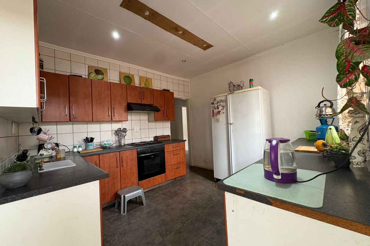 Functional kitchen featuring wooden cabinetry, tiled backsplash, built-in oven and hob, and dark tiled flooring, offering a practical layout for daily meal preparation.