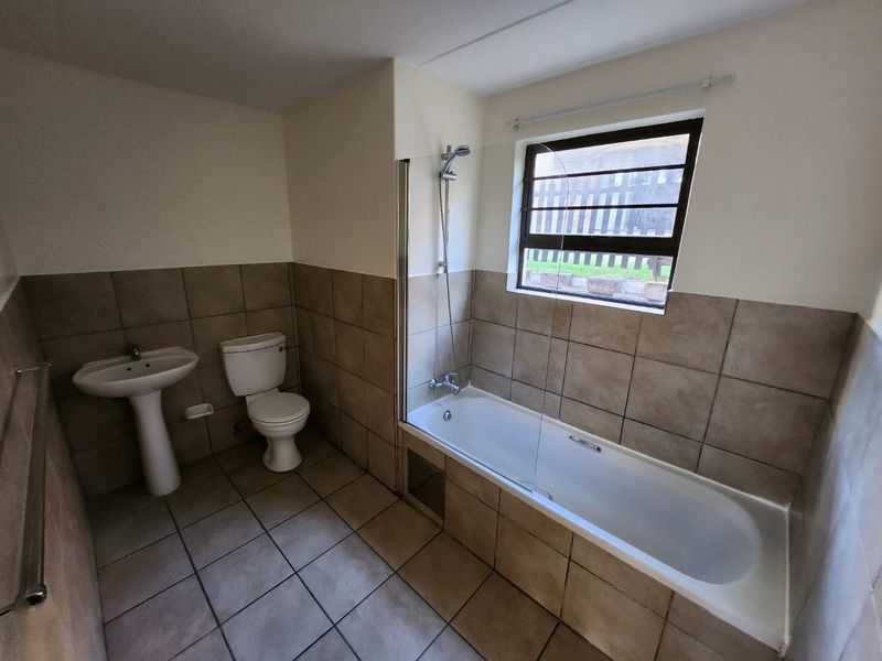 A functional bathroom featuring a pedestal basin, toilet, and a bathtub with a shower mixer and glass screen, finished with neutral wall and floor tiles.