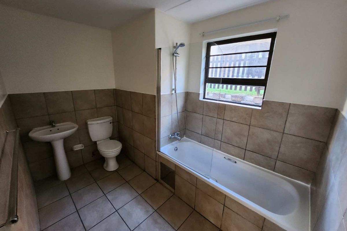 A functional bathroom featuring a pedestal basin, toilet, and a bathtub with a shower mixer and glass screen, finished with neutral wall and floor tiles.
