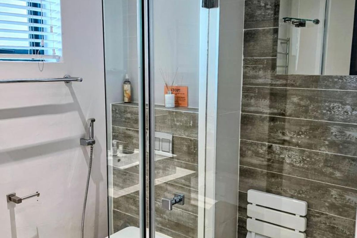 Modern bathroom featuring a glass-enclosed shower with a rain shower head, wall-mounted toilet, and stylish wood-look tile accents.