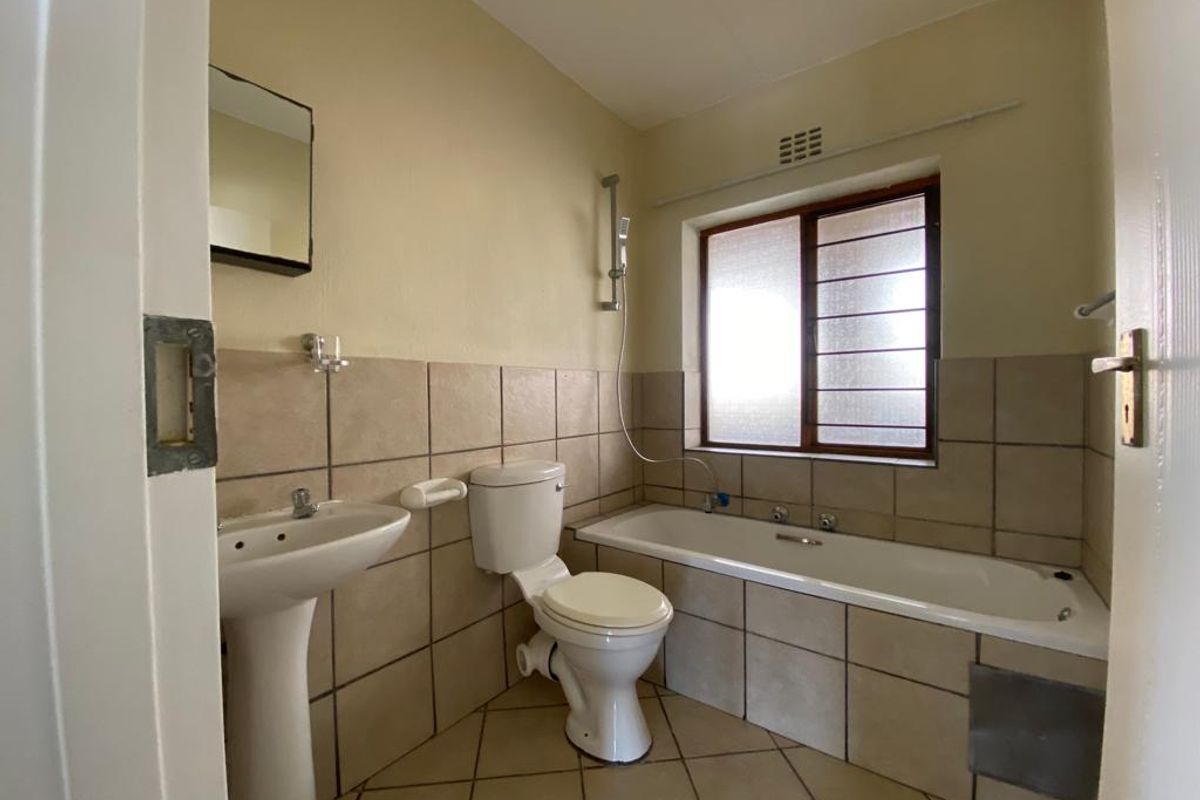 A functional bathroom featuring a pedestal basin, toilet, and a bathtub with a shower attachment, finished with neutral wall and floor tiling.