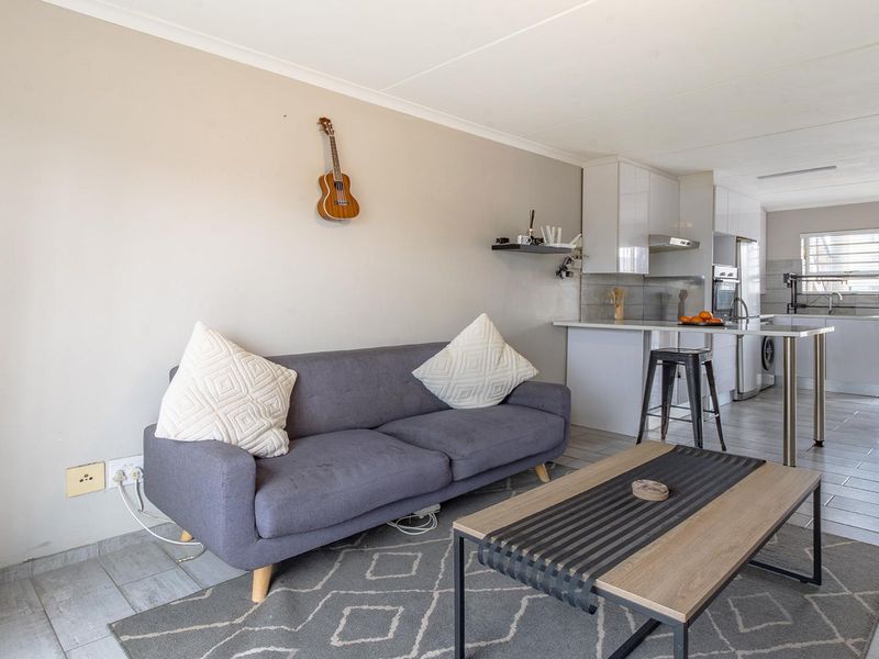 An open-plan living area featuring a modern kitchen with built-in cabinetry and tiled flooring throughout, creating a seamless flow between the kitchen and lounge.